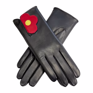 A pair of women's black Italian aniline leather gloves displayed on a white background. Each glove features a unique red leather strap fastened with velcro in the shape of a flower, complete with a bright yellow leather circle in the center.